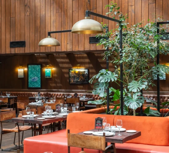 Espacio interior de Rubaiyat definido por materiales nobles, tonos tierra y detalles en cobre, articulado en torno a una plaza central con vegetación, arte contemporáneo e iluminación cálida de producción local.